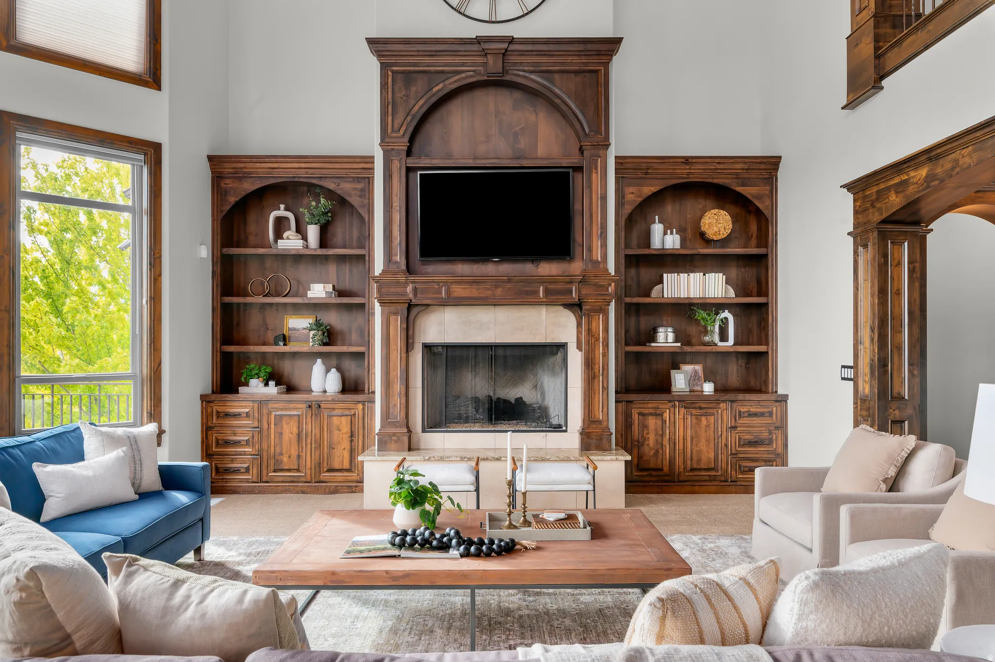 Expansive living area with a stone fireplace, built-in wooden shelving, and large windows