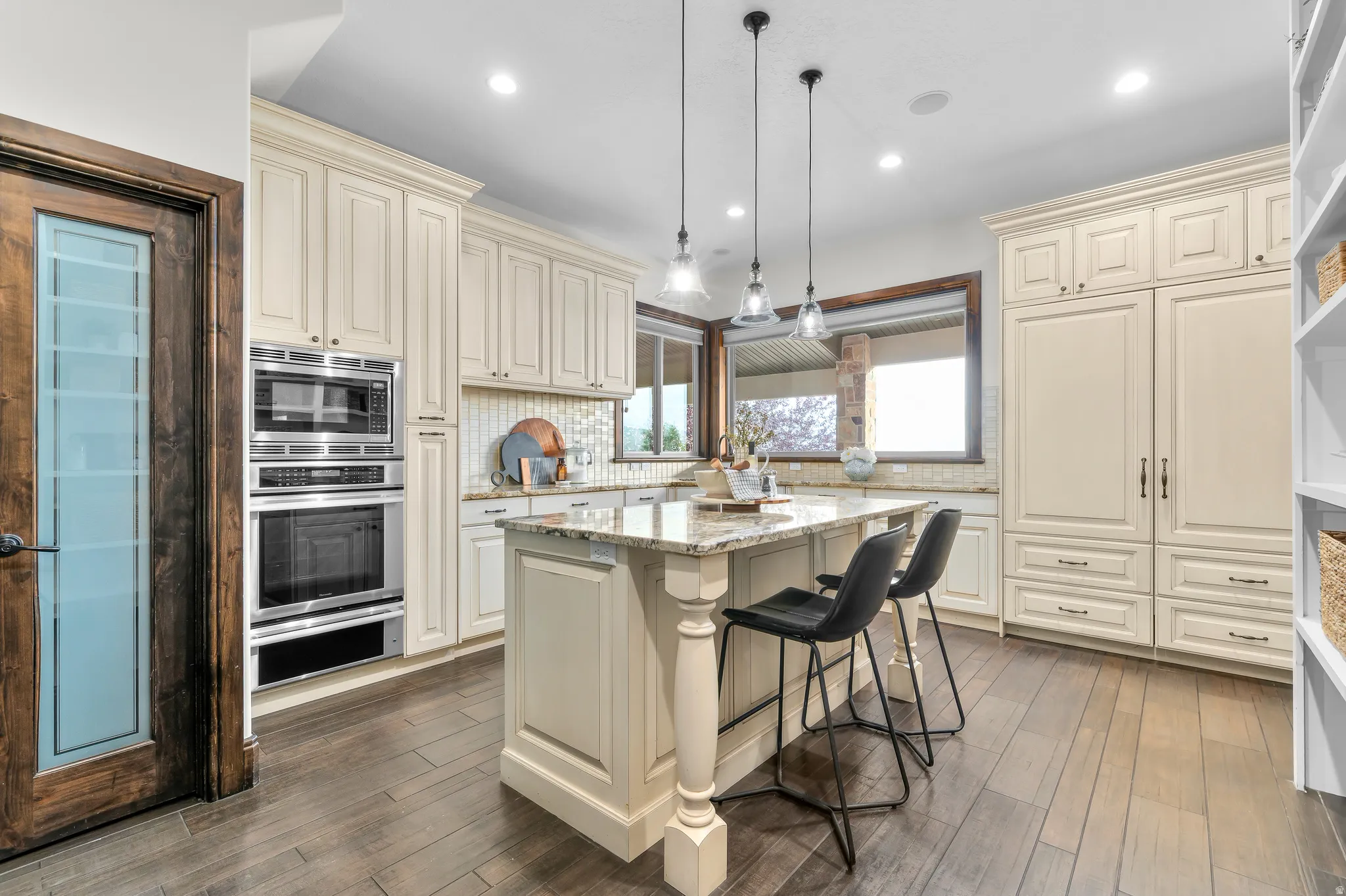 Kitchen featuring a large central island with granite countertop, integrated stainless steel double oven, white shaker cabinetry, and wood-finish flooring