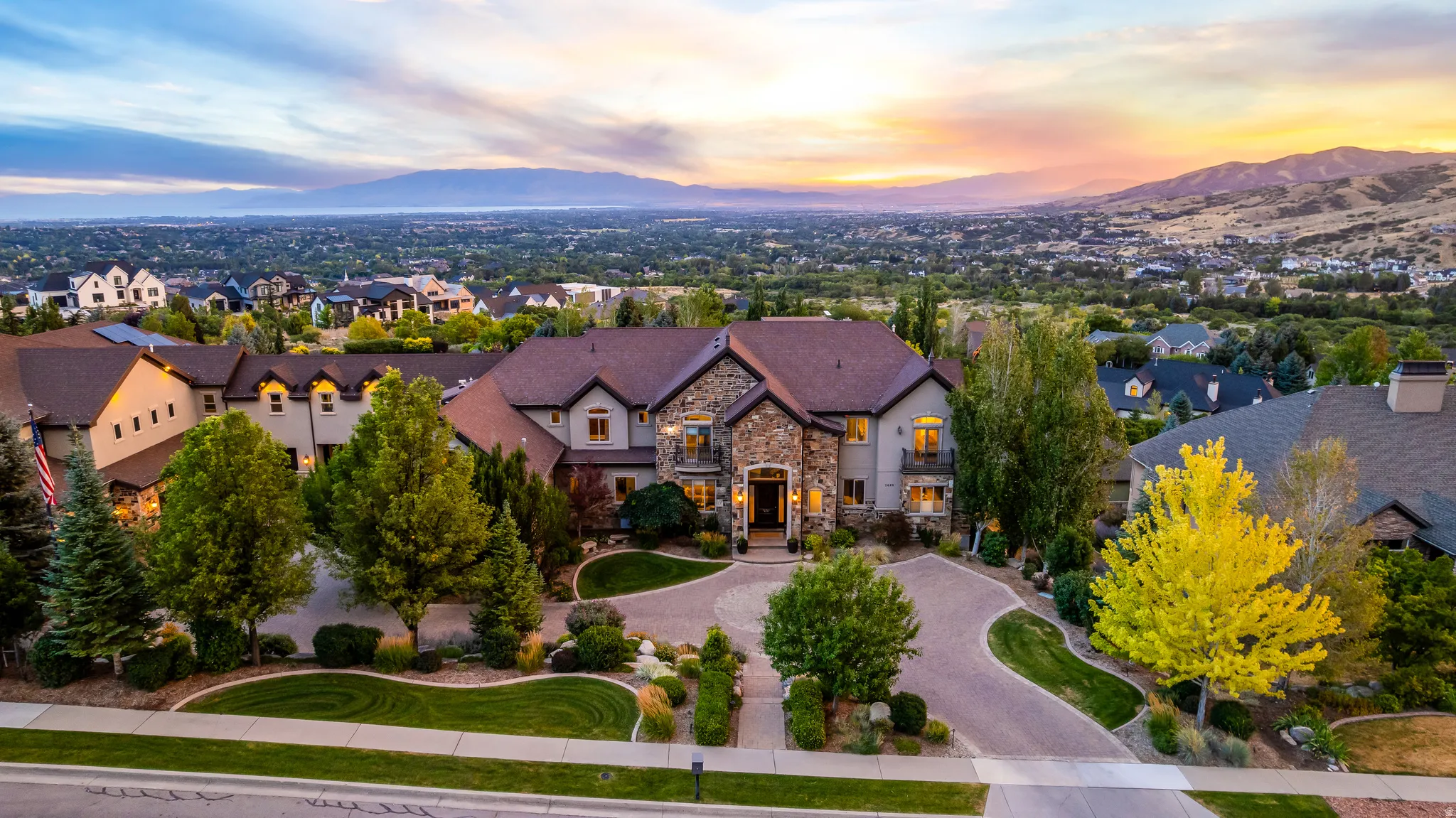 Expansive residence featuring a stone and stucco exterior, multiple gabled rooflines, a circular paver driveway, and mature landscaping