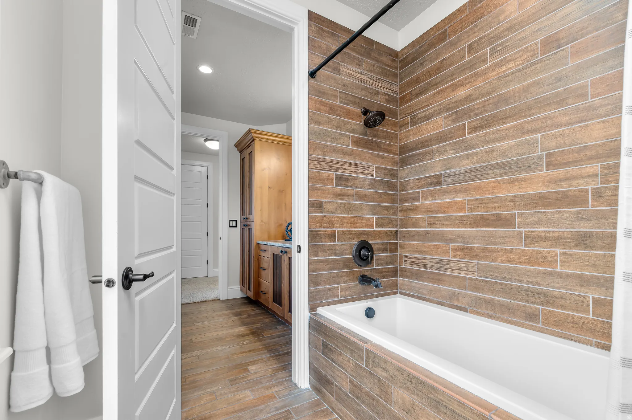 Bathtub with wood-look tile surround and matte black fixtures