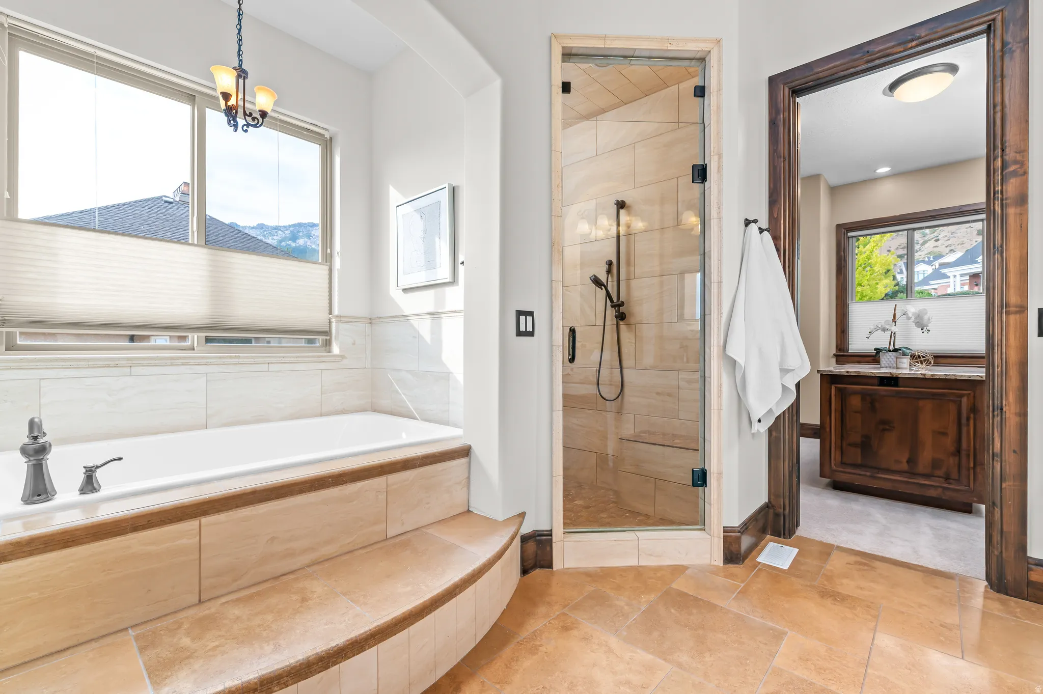 Soaking tub with tile surround, glass-enclosed shower, wood-finish flooring, and a large window with privacy shades