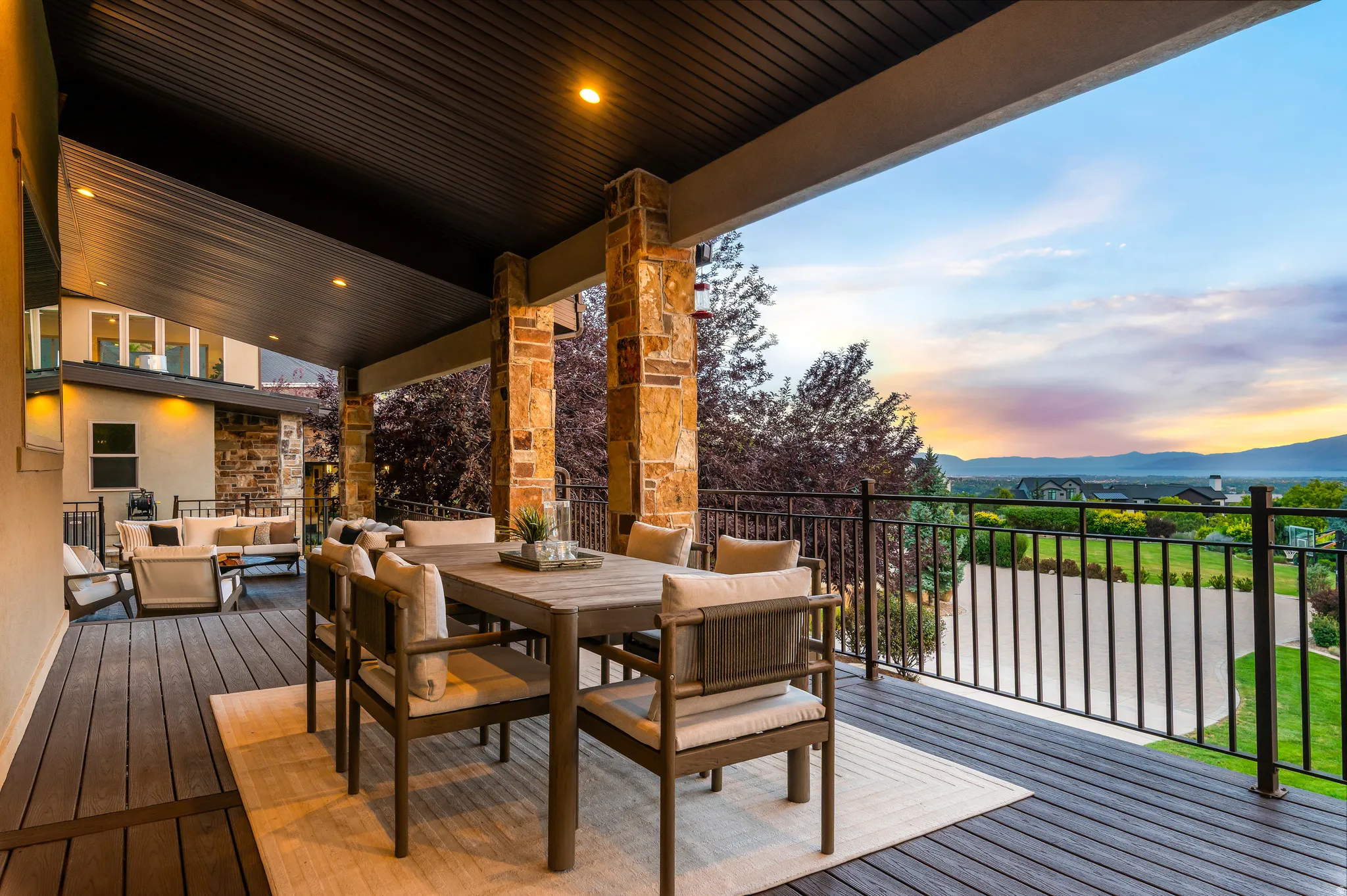 Covered outdoor deck with composite decking, recessed lighting, stone columns, and a black metal railing
