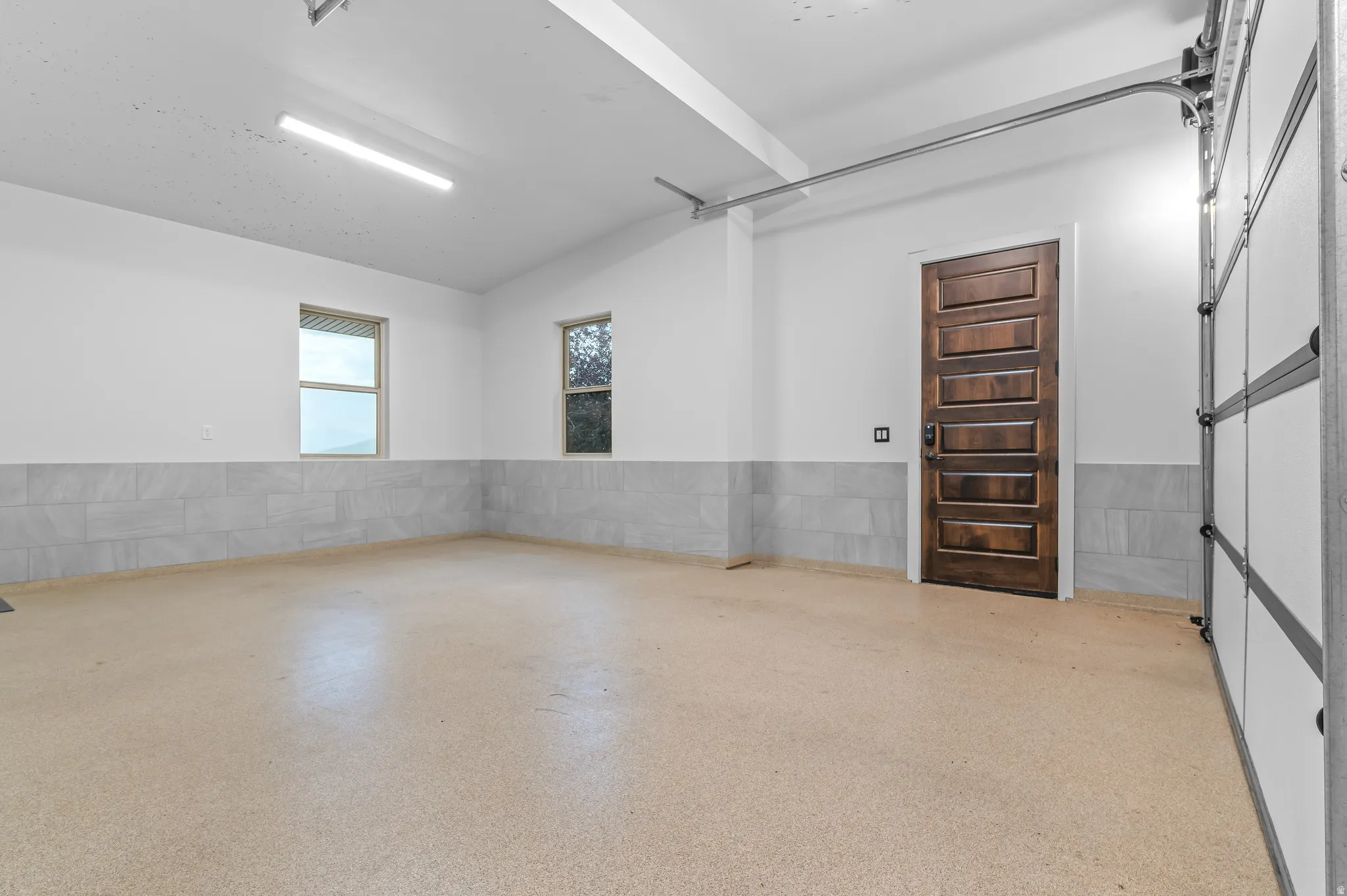 Smooth epoxy flooring, two windows, recessed lighting, wood-paneled interior door, and a paneled overhead garage door
