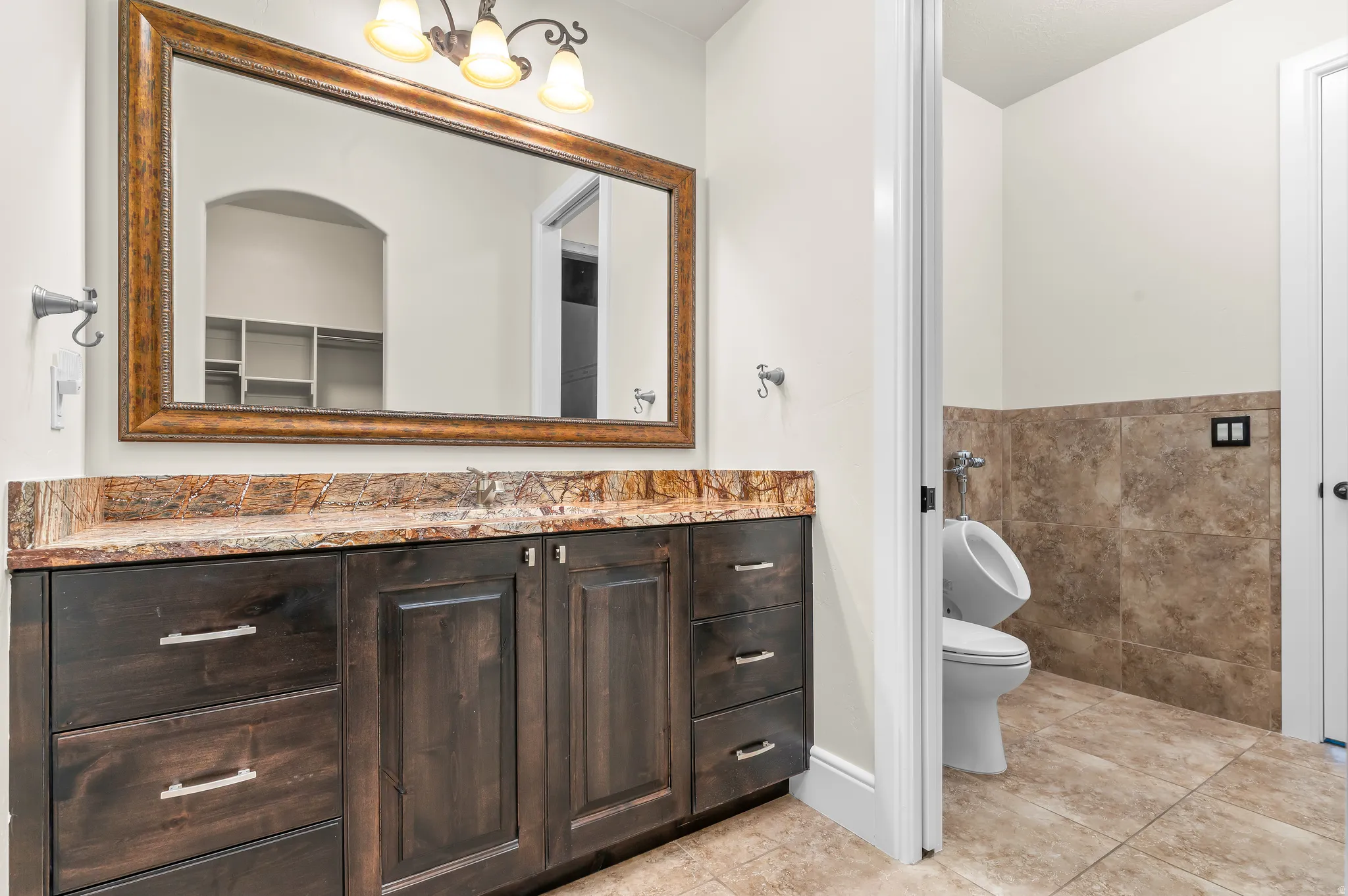 Dark wood-finish vanity with a stone countertop, framed mirror, and three-light vanity fixture