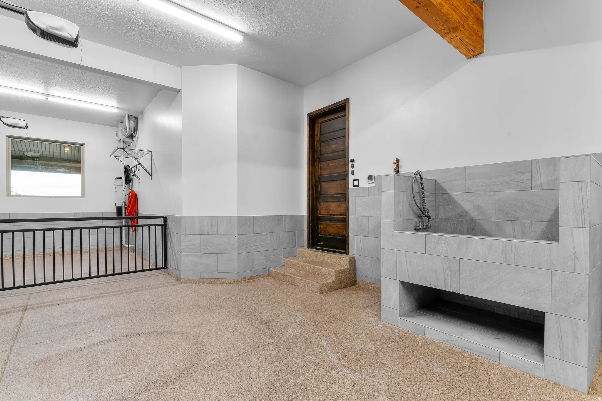 Utility area featuring a tiled wash station with a faucet, a solid wood door, and exposed wood ceiling beams