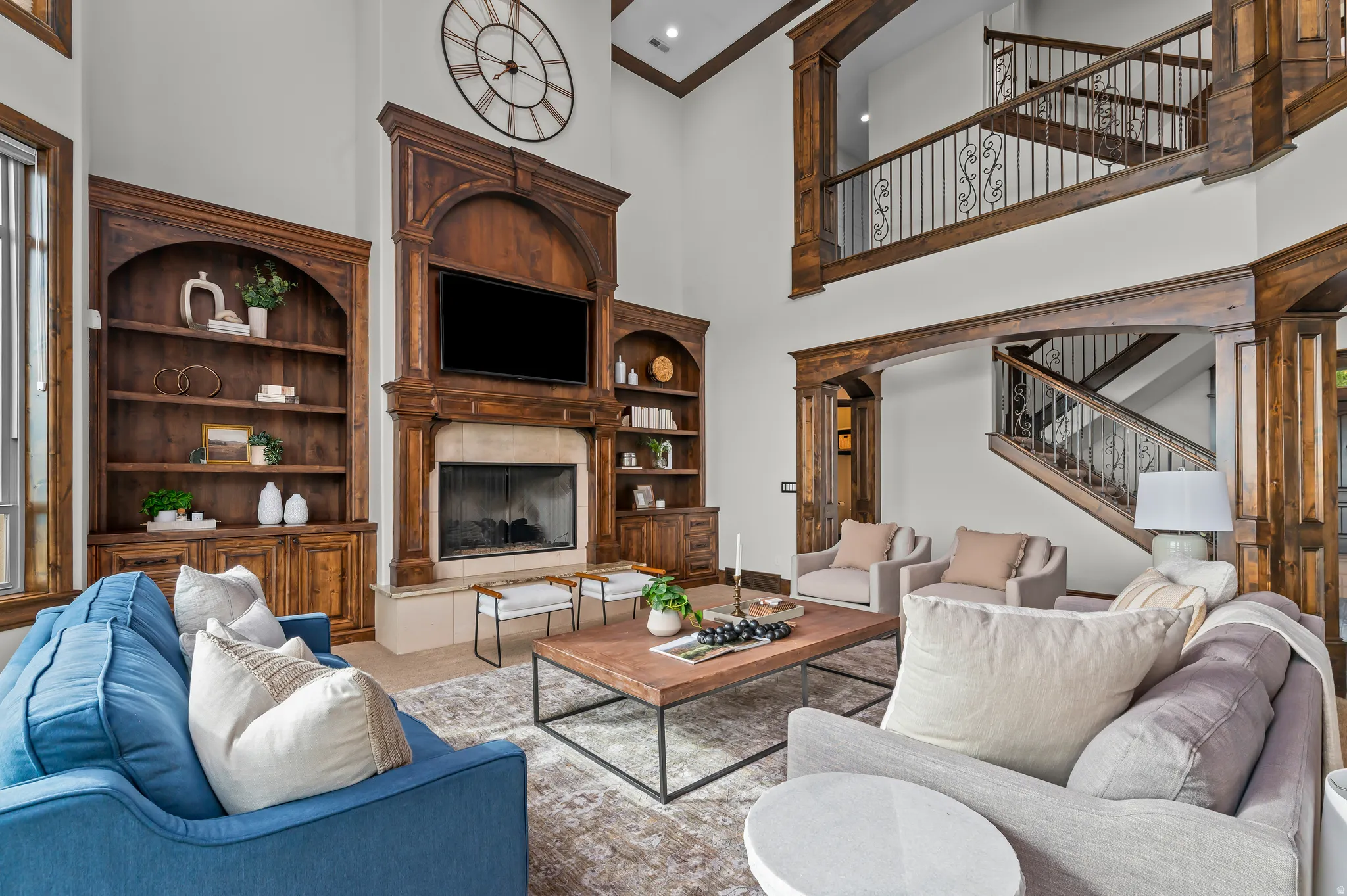 Two-story living area with a stone fireplace, built-in shelving, wood-beam accents, and a staircase featuring decorative ironwork