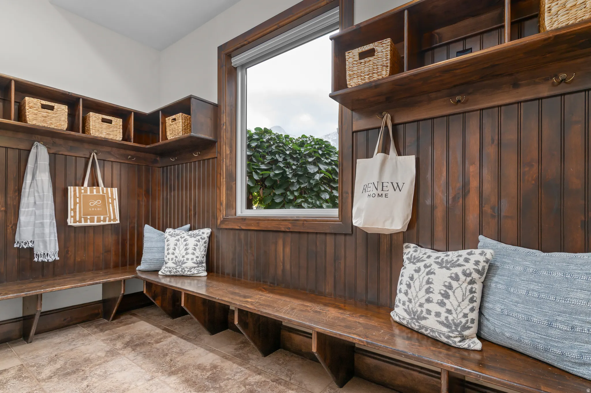 Built-in wood-finish bench with overhead shelving, wall hooks, and beadboard paneling