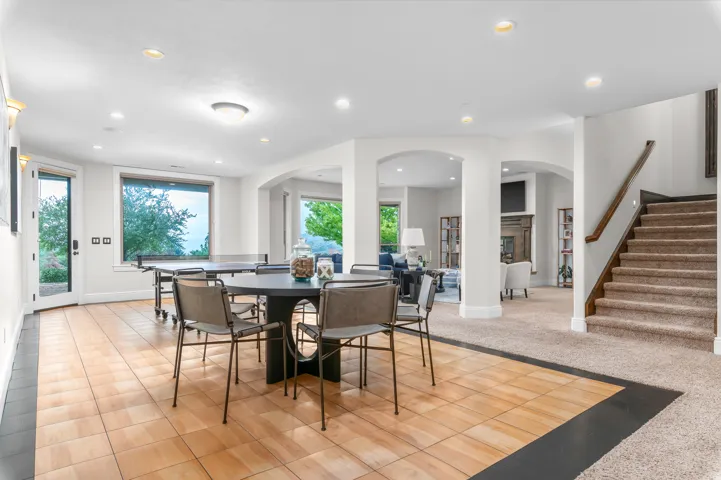 Lower level featuring mixed flooring, arched doorways, multiple recessed lights, a glass-paned exterior door, and a carpeted staircase with wood railing