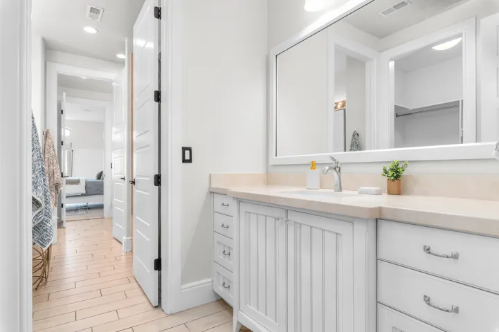 Vanity with a polished chrome faucet, stone countertop, integrated sink, and white cabinetry featuring both drawers and beadboard doors