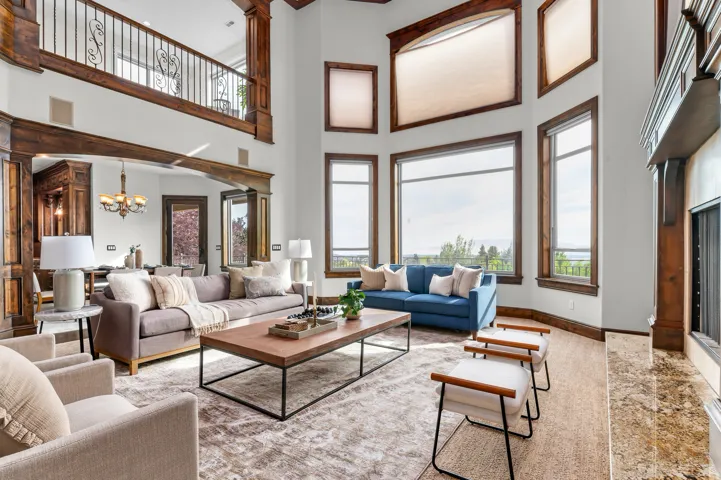Two-story great room featuring a prominent fireplace with a stone hearth, extensive wood-finish trim and beams, and large windows with transom elements