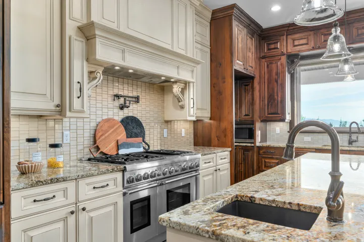 Gourmet kitchen featuring a stainless steel range, light-toned cabinetry, dark wood-finish cabinetry, patterned tile backsplash, and stone countertops