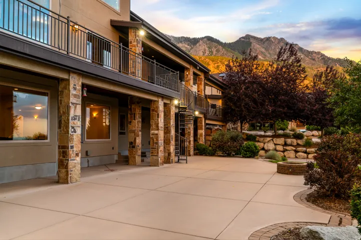 Expansive concrete patio with a built-in fire pit, stone-clad columns, and a terraced rock garden