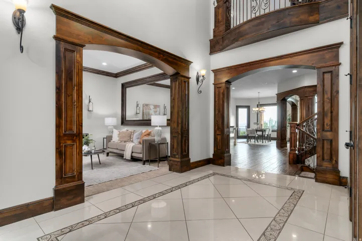 Entryway with large format tile flooring featuring an intricate mosaic border, rich wood-stained arched doorways, and a grand staircase with decorative wrought iron balusters