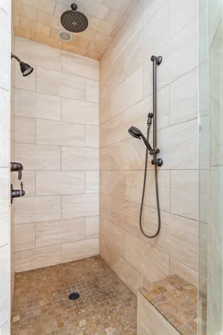 Walk-in shower with neutral-toned wall tiling, mosaic tile floor, built-in bench, and dual shower heads