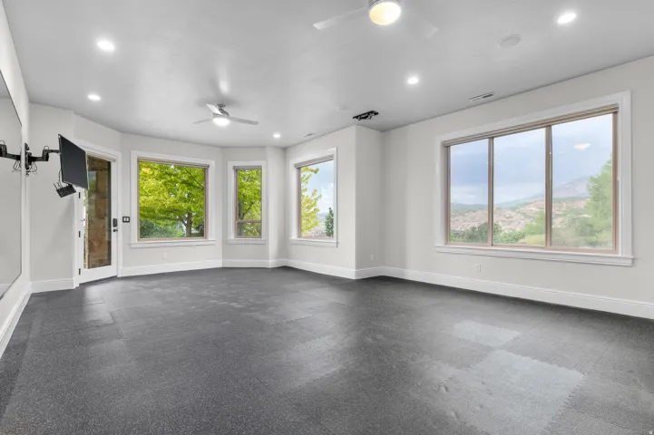 Fitness room, Recessed lighting, ceiling fans, hard surface flooring, multiple large windows, and a glass-paneled door