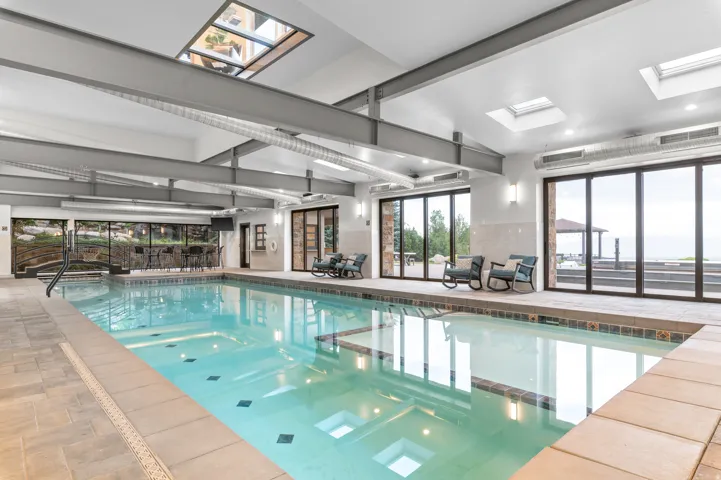 Indoor swimming pool with integrated spa, multiple skylights, full-height glass doors, and exposed ceiling beams