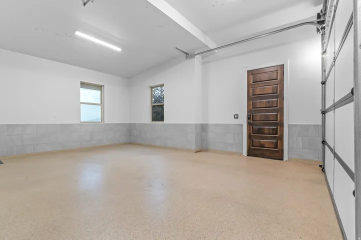 Smooth epoxy flooring, two windows, recessed lighting, wood-paneled interior door, and a paneled overhead garage door