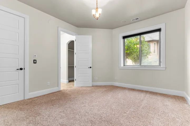 Plush carpet flooring, neutral painted walls, a built-in closet with shelving, a white-framed window, and a decorative chandelier