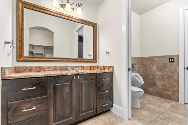 Dark wood-finish vanity with a stone countertop, framed mirror, and three-light vanity fixture