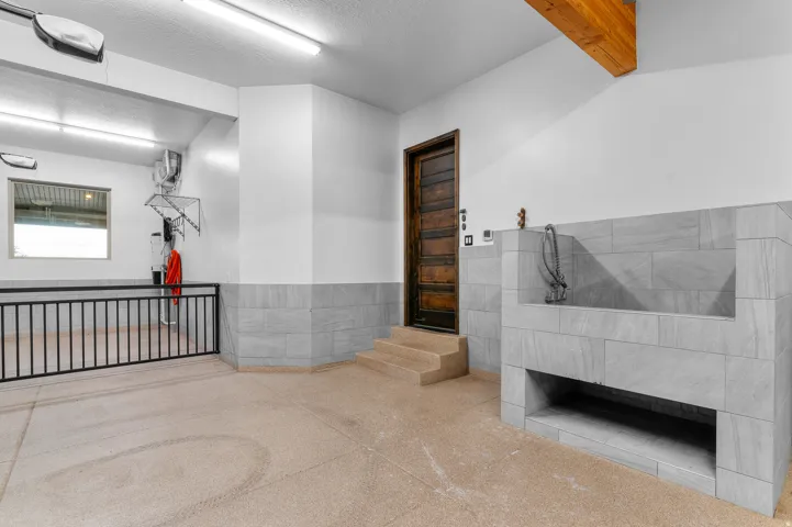 Utility area featuring a tiled wash station with a faucet, a solid wood door, and exposed wood ceiling beams