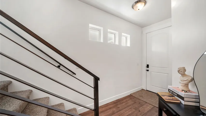 Wood-finish flooring, white arched panel door, and modern horizontal metal railing