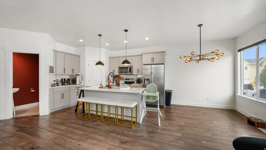Open-concept living space featuring wood-finish flooring, a kitchen island with pendant lighting, stainless steel appliances, and large windows