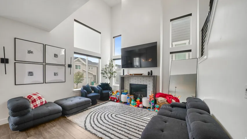 Bright, open living area showcasing soaring ceilings with skylight, custom framed artwork, gas fireplace with mantel, geometric area rug, wood-finish flooring, and abundant natural light from oversized windows