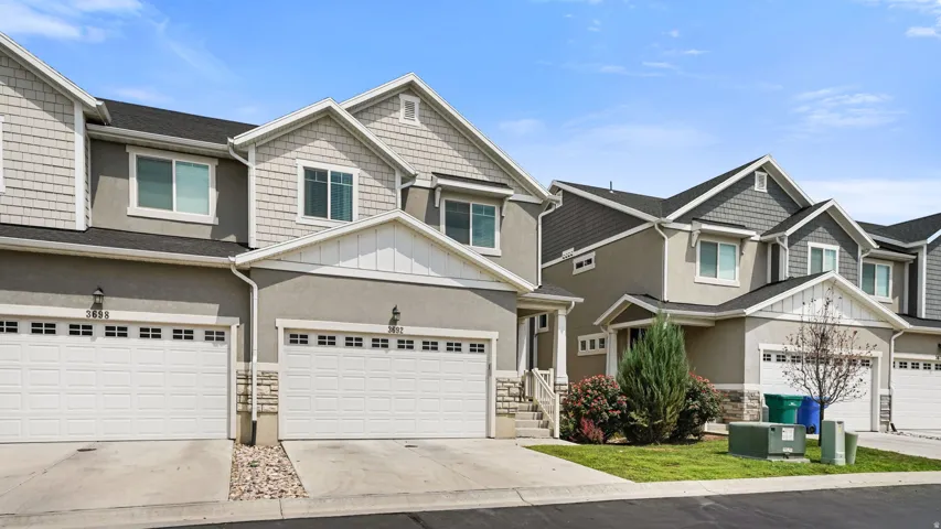 Contemporary townhome exterior featuring shingle and stucco siding, dual garage doors, and a stone accent facade