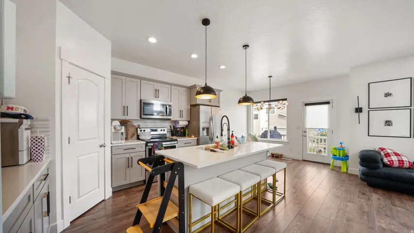 Modern kitchen featuring light gray cabinetry, stainless steel appliances, a white island with seating, and wood-finish flooring