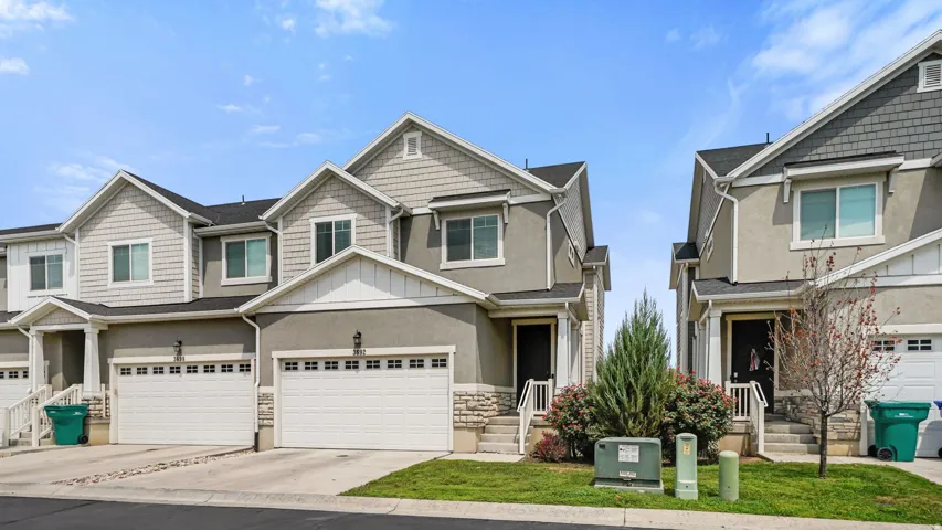 Contemporary townhome featuring a stucco and shingle exterior, attached two-car garage, covered entry, and manicured landscaping