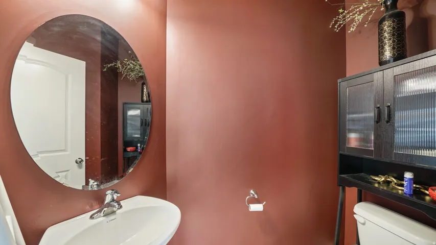 Main Floor - Wall-mounted oval mirror, white pedestal sink with chrome faucet, black storage cabinet with reeded glass doors, and a white toilet