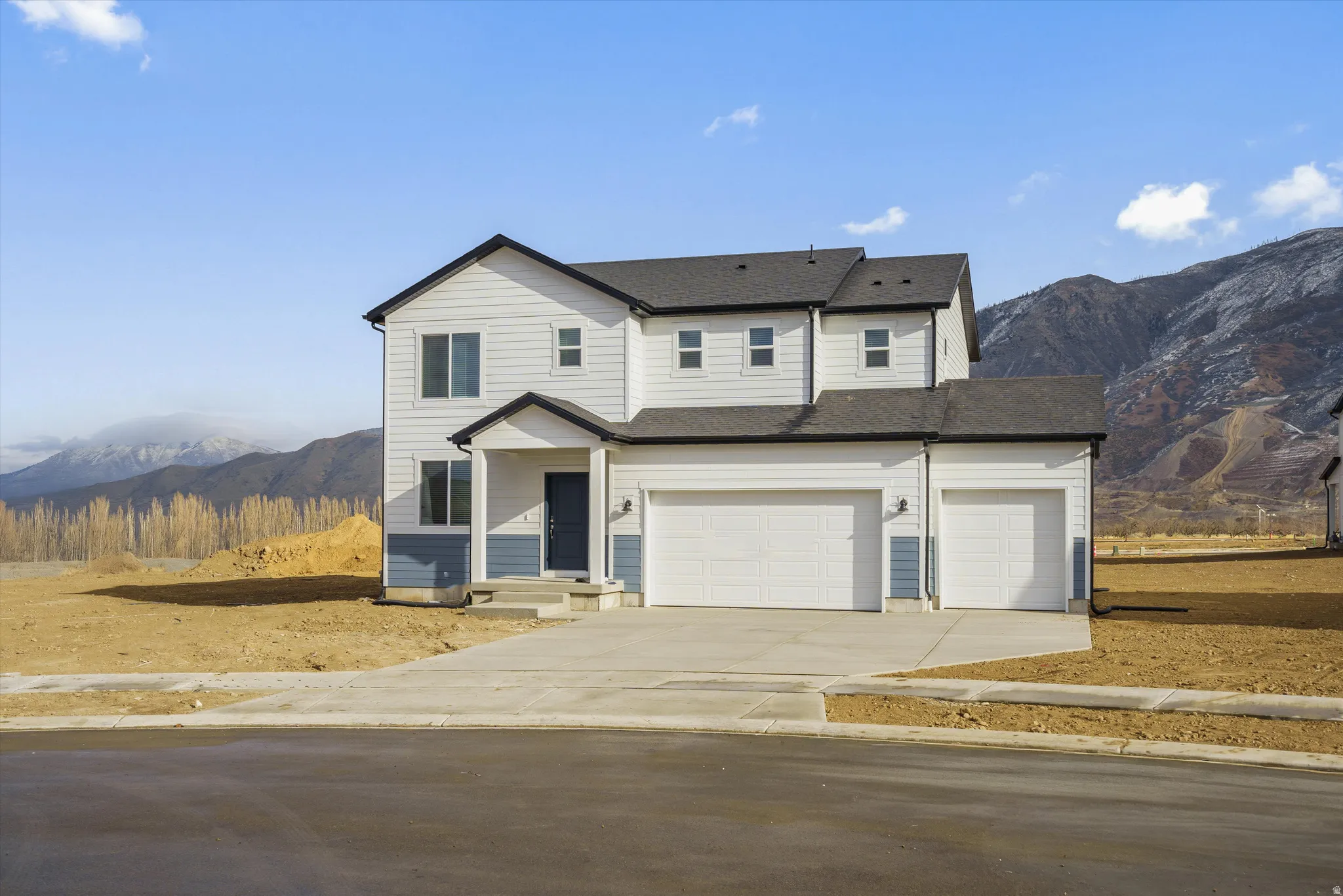 Two-story residence featuring white and blue siding, a dark shingle roof, an attached two-car garage, an additional single-car garage, and a concrete driveway