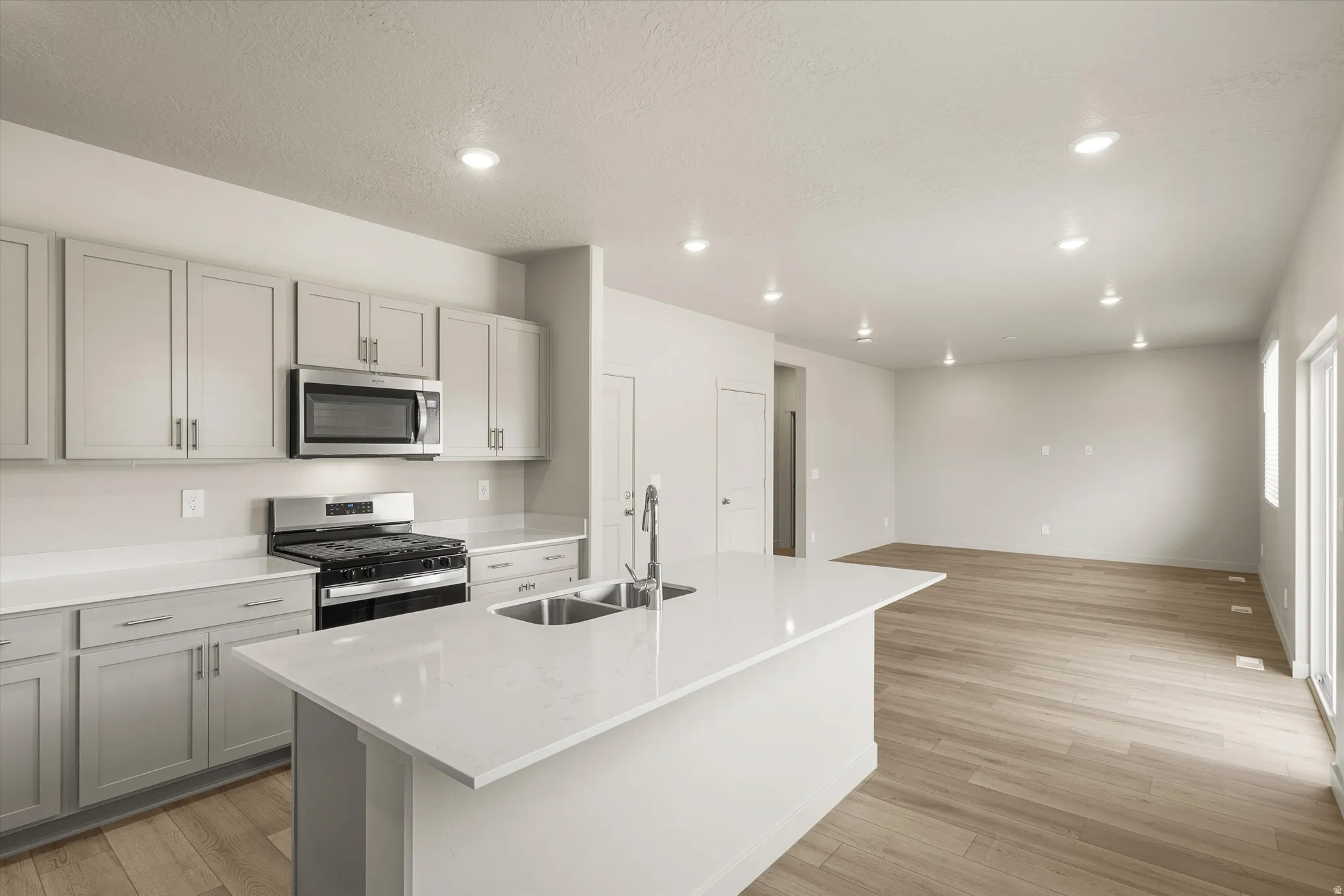 **DISCLAIMER** This floorplan has upgrades not photographed.Spacious kitchen featuring an island with a double basin sink, stainless steel appliances, light gray cabinetry, and light-toned countertops