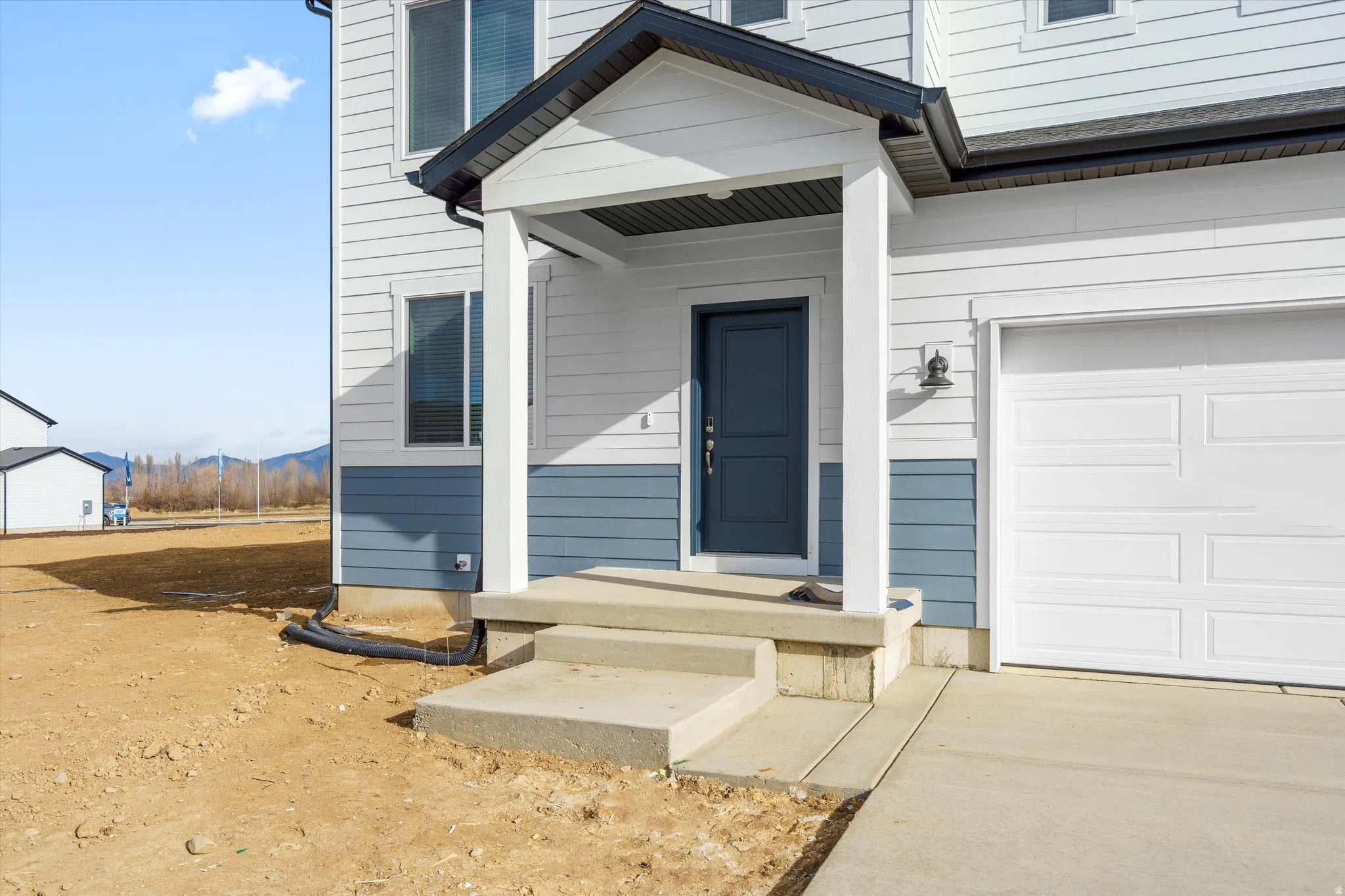 Two-story exterior with horizontal siding, covered entry porch, dark blue entry door, and attached garage with white door