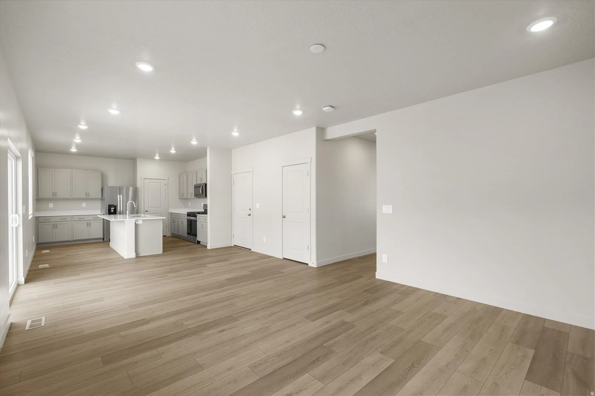 **DISCLAIMER** This floorplan has upgrades not photographed.Expansive open-concept living area with wood-finish flooring, recessed lighting, and a kitchen island with a sink
