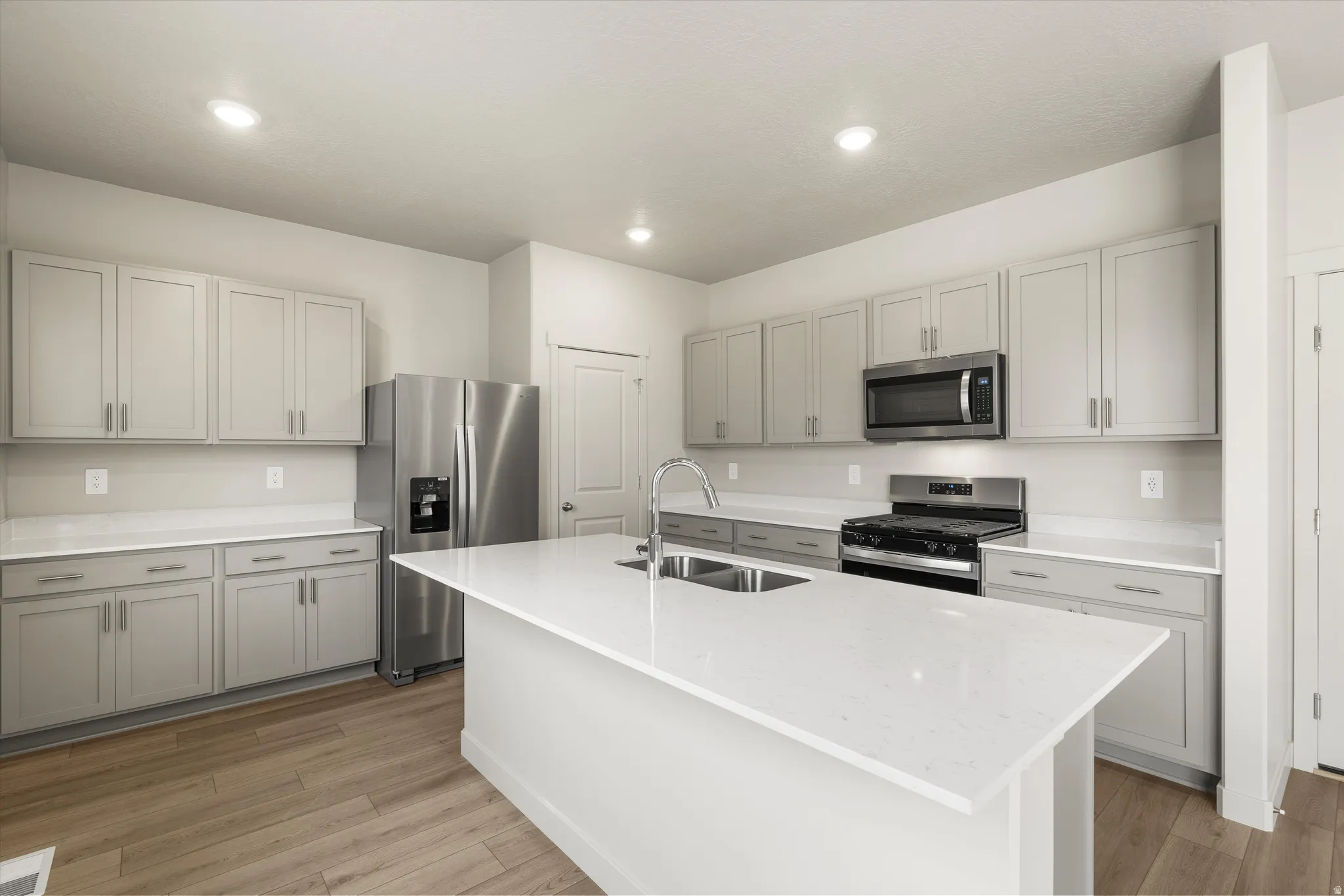 **DISCLAIMER** This floorplan has upgrades not photographed.Kitchen featuring light-toned cabinetry, light-toned countertops, stainless steel appliances, a center island with an integrated sink, and wood-finish flooring