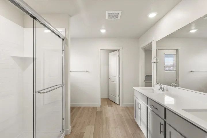 **DISCLAIMER** This floorplan has upgrades not photographed.Dual vanity with integrated sinks, wood-finish flooring, glass-enclosed shower, white subway tile shower surround, and recessed lighting