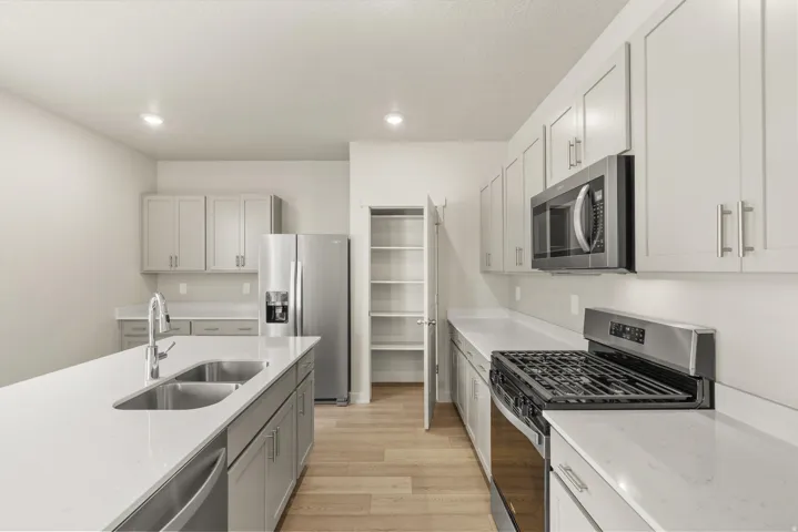 **DISCLAIMER** This floorplan has upgrades not photographed.Kitchen featuring light-finish cabinetry, stainless steel appliances, light-toned countertops, a kitchen island with a double basin sink, and wood-finish flooring