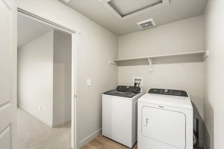 **DISCLAIMER** This floorplan has upgrades not photographed.Dedicated laundry area featuring wood-finish flooring, a white wall-mounted shelf, and light-toned walls