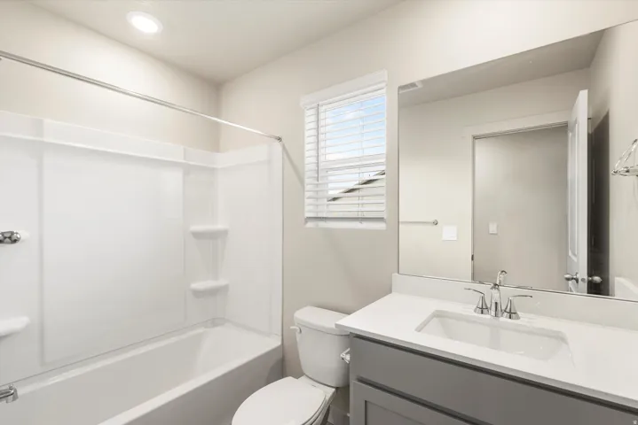 **DISCLAIMER** This floorplan has upgrades not photographed.Recessed lighting, white composite bathtub and shower surround, light gray vanity with white countertop, chrome fixtures, and a window with blinds