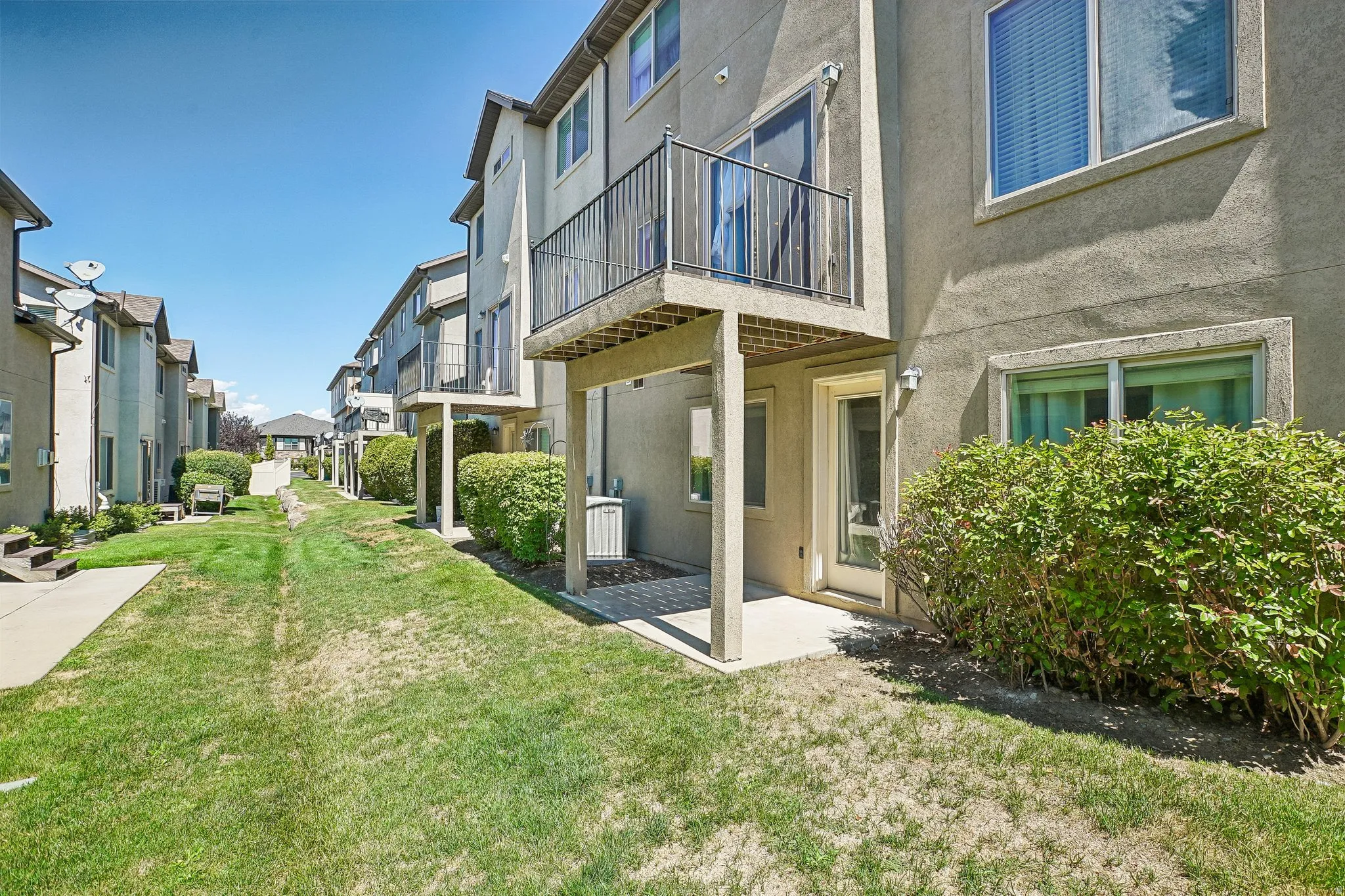 Two-story townhouse exterior with stucco finish, private balcony, ground-level patio, and adjacent green space