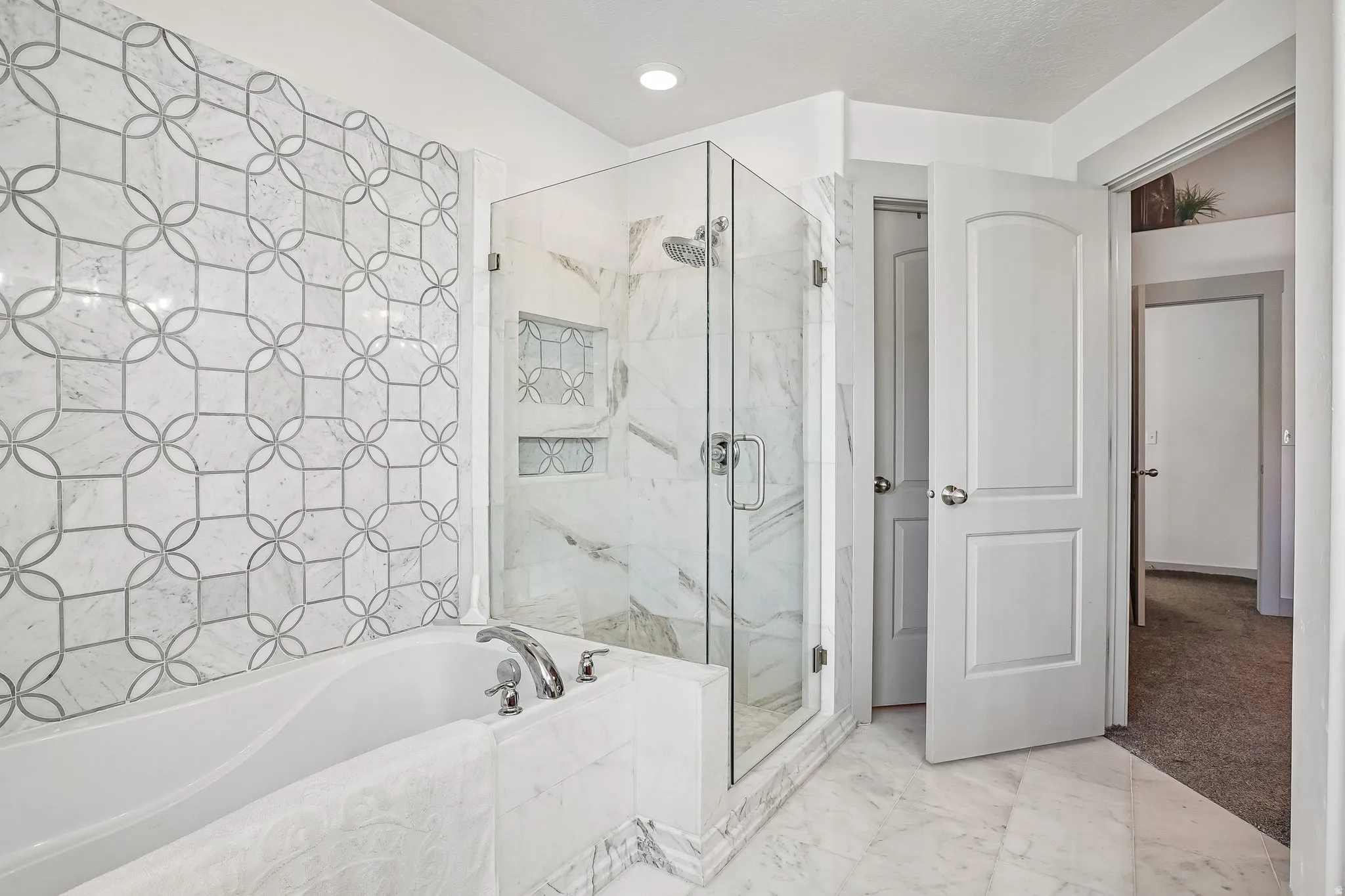 Tiled shower with glass enclosure and built-in niches, separate soaking tub with decorative tiled surround, and white panel doors