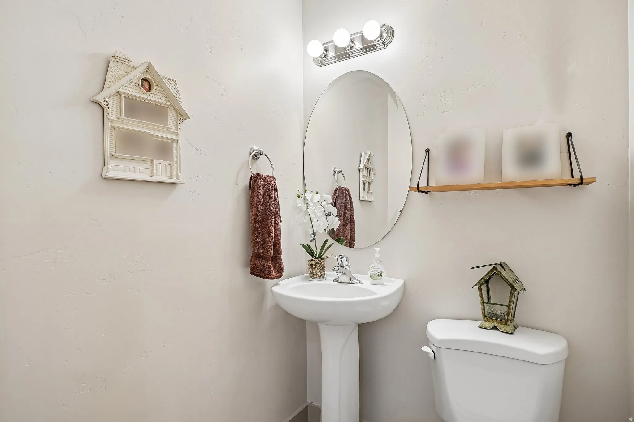 Pedestal sink with chrome faucet, oval mirror, and wall-mounted light fixture
