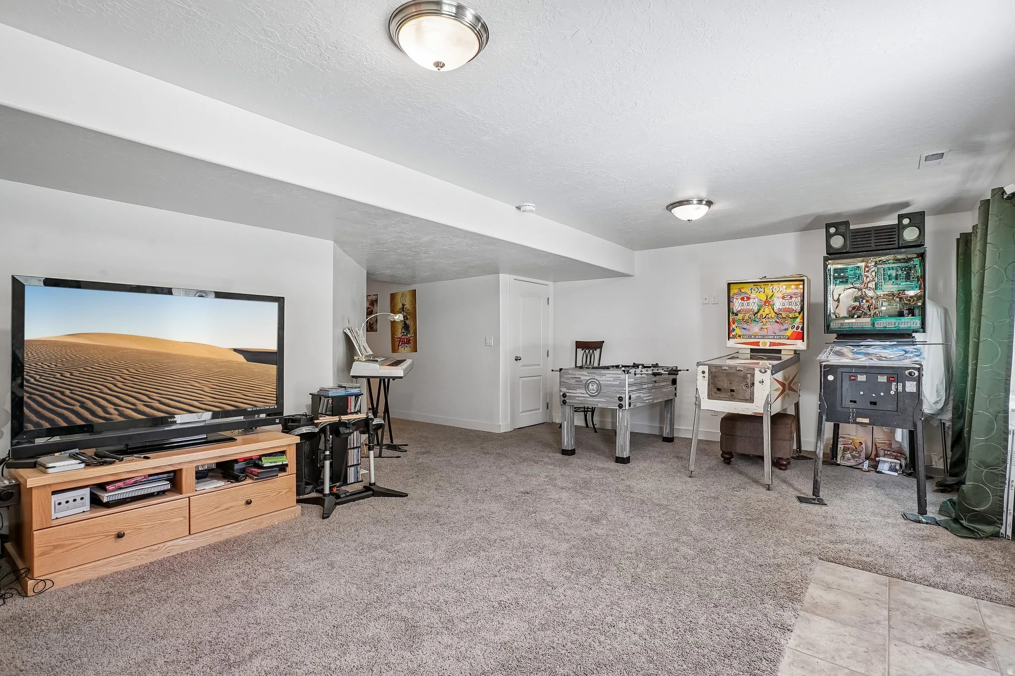 Carpeted floor, recessed ceiling beam, flush-mount lighting, white interior door, and a partially visible tiled area