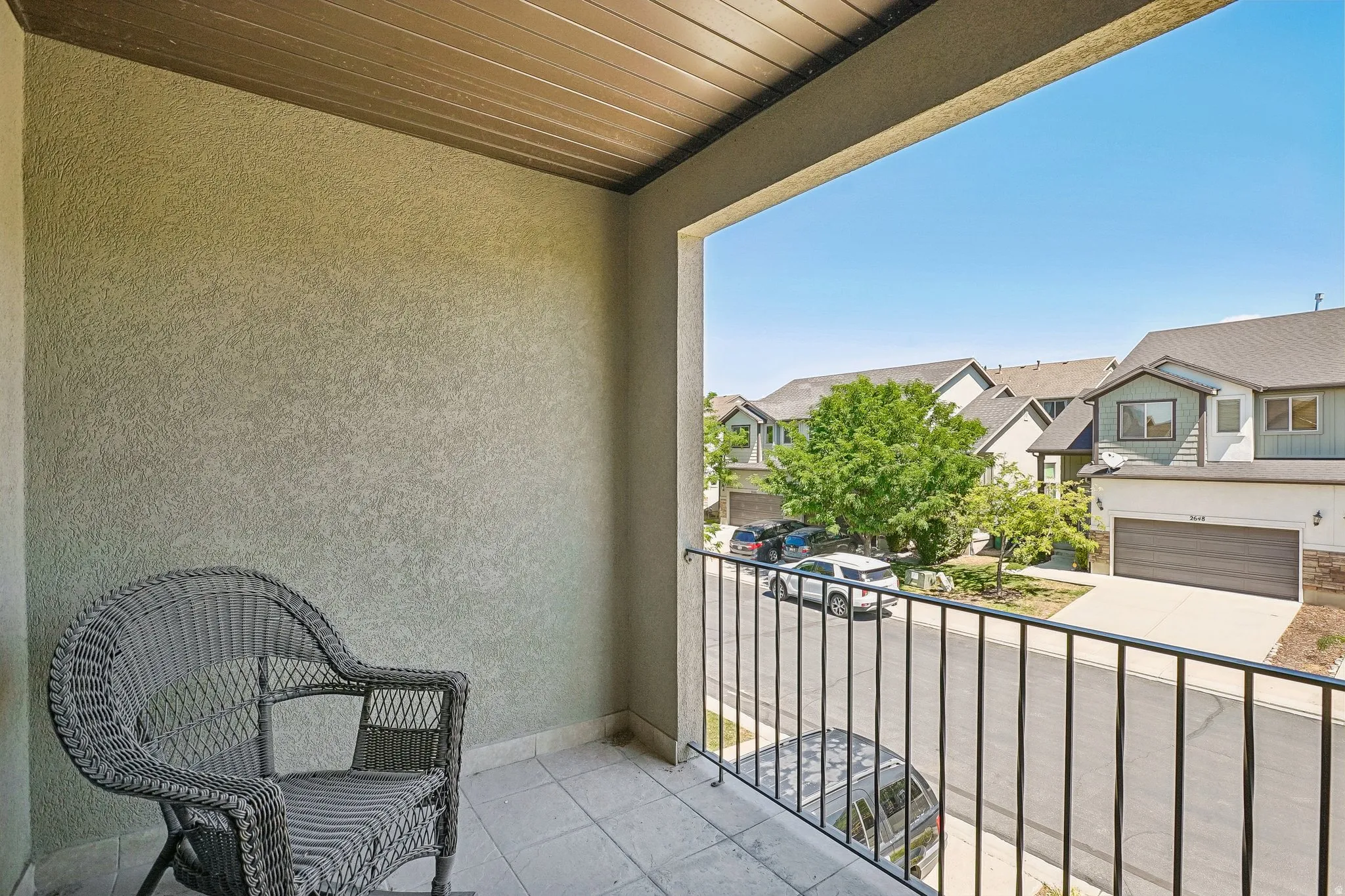 Covered balcony featuring a wood-finish ceiling, textured stucco walls, and metal railing overlooking the neighborhood streetscape