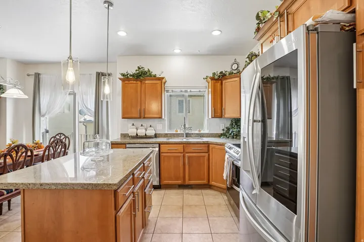 Kitchen featuring wood cabinetry, stone-finish countertops, stainless steel appliances, and tile flooring
