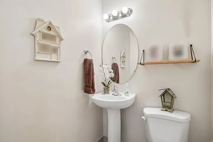 Pedestal sink with chrome faucet, oval mirror, and wall-mounted light fixture