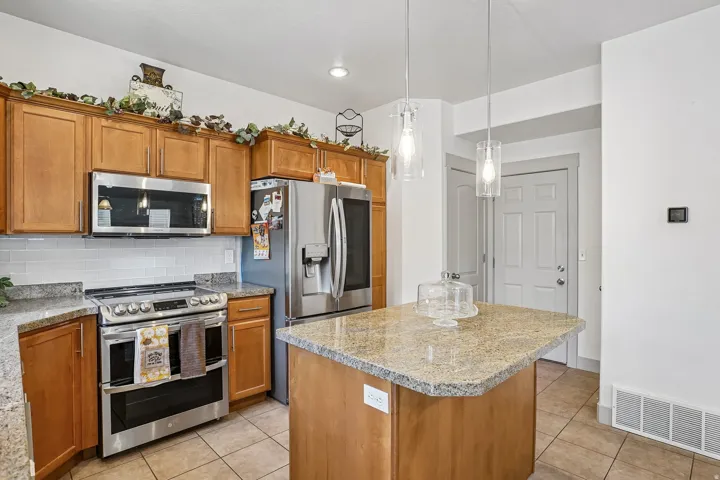 Kitchen featuring wood cabinetry, stainless steel appliances, granite countertops, and a subway tile backsplash