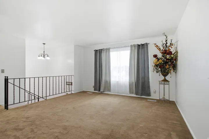 Carpeted living space featuring a window with natural light, white walls, and a chandelier-style light fixture