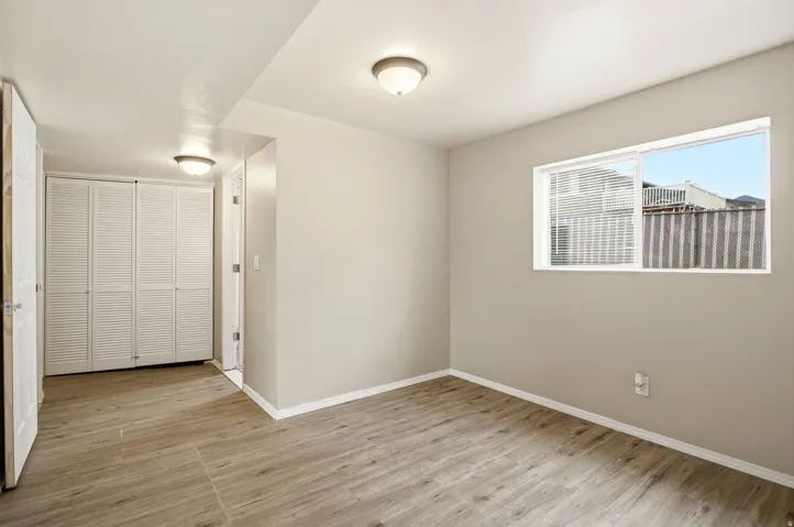 Wood-finish flooring, white walls, white bi-fold closet doors, and a window with white blinds